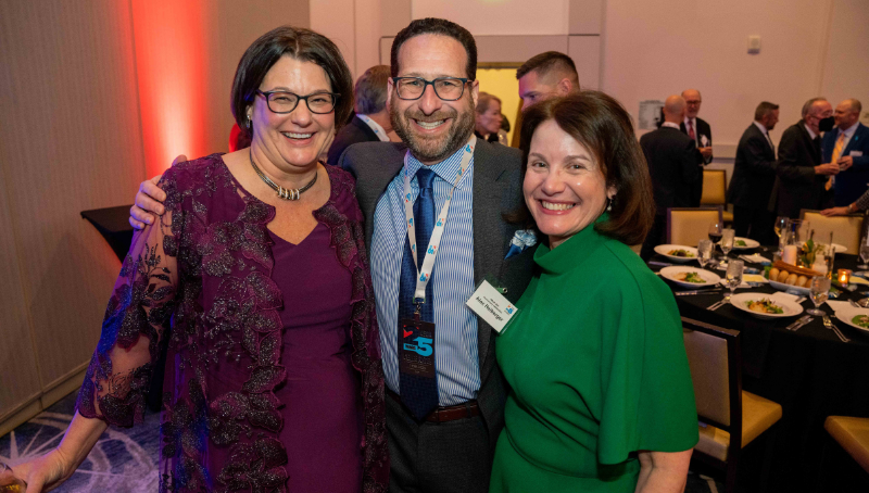 Two dressed up women standing on either side of a dressed up man